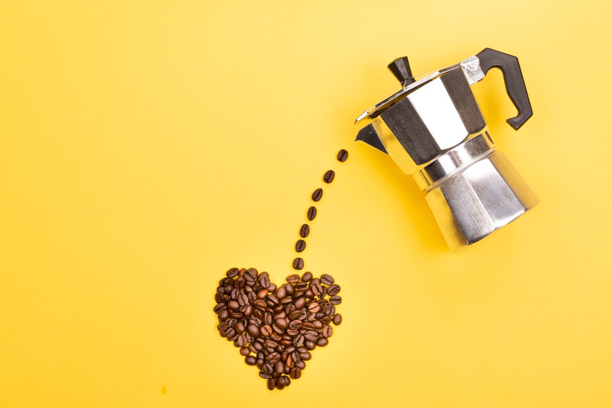 Coffee beans pouring from coffee maker into a heart shape on yellow background. Love coffee concept. Flat-lay, top view.