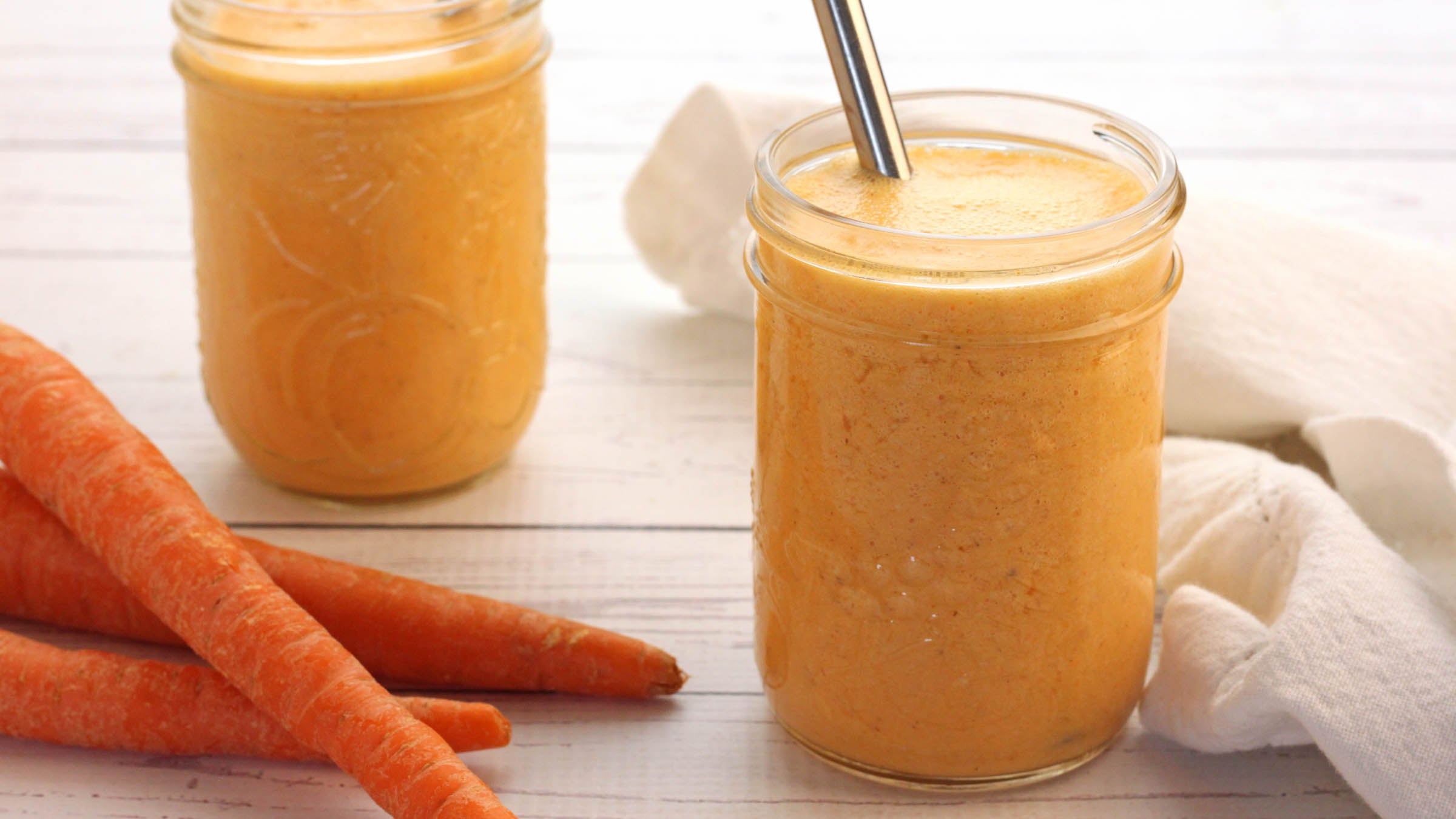 Two mason jars of mango carrot smoothie next to whole carrots