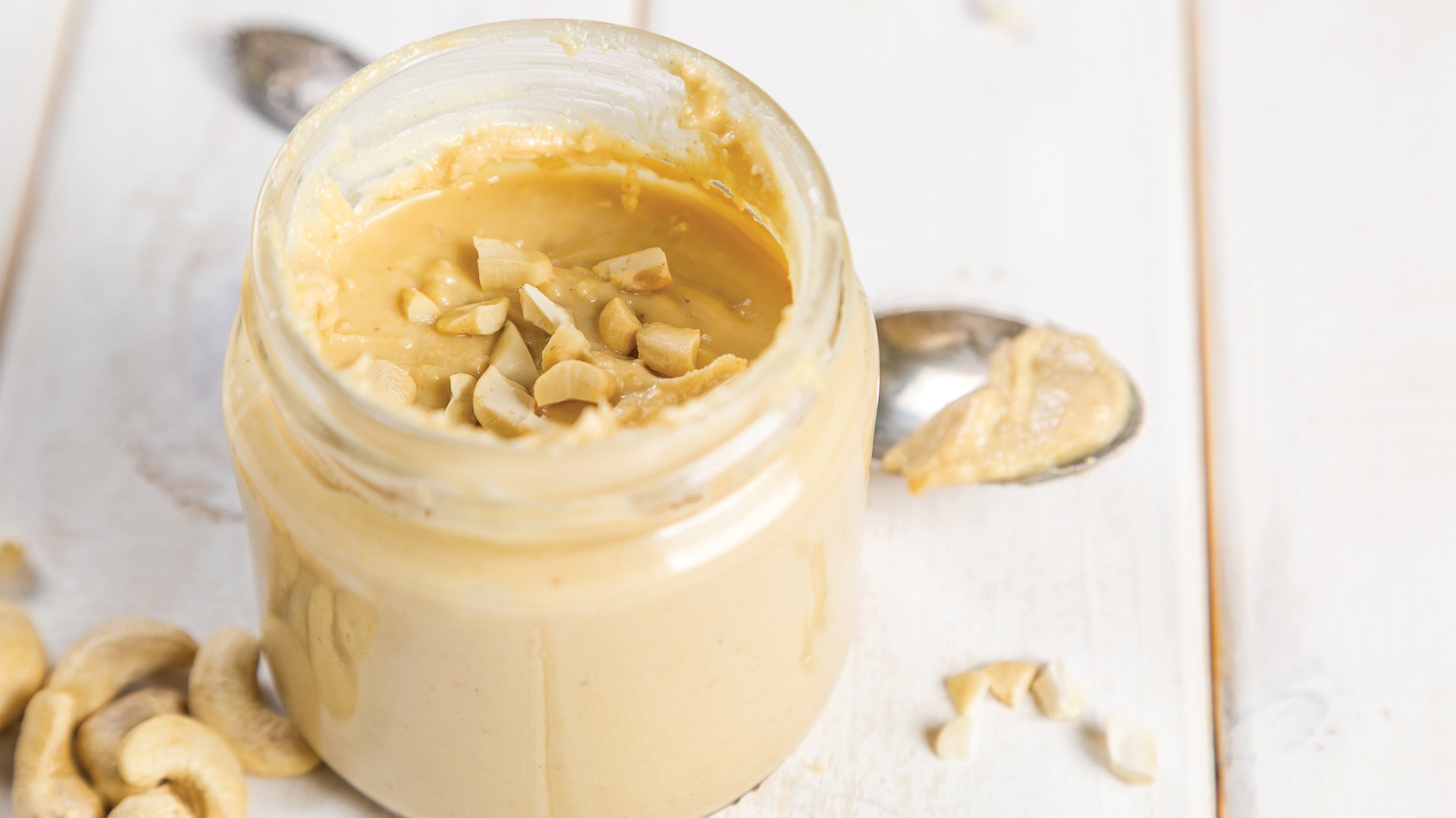 Cashew butter in glass jar with cashews and spoon